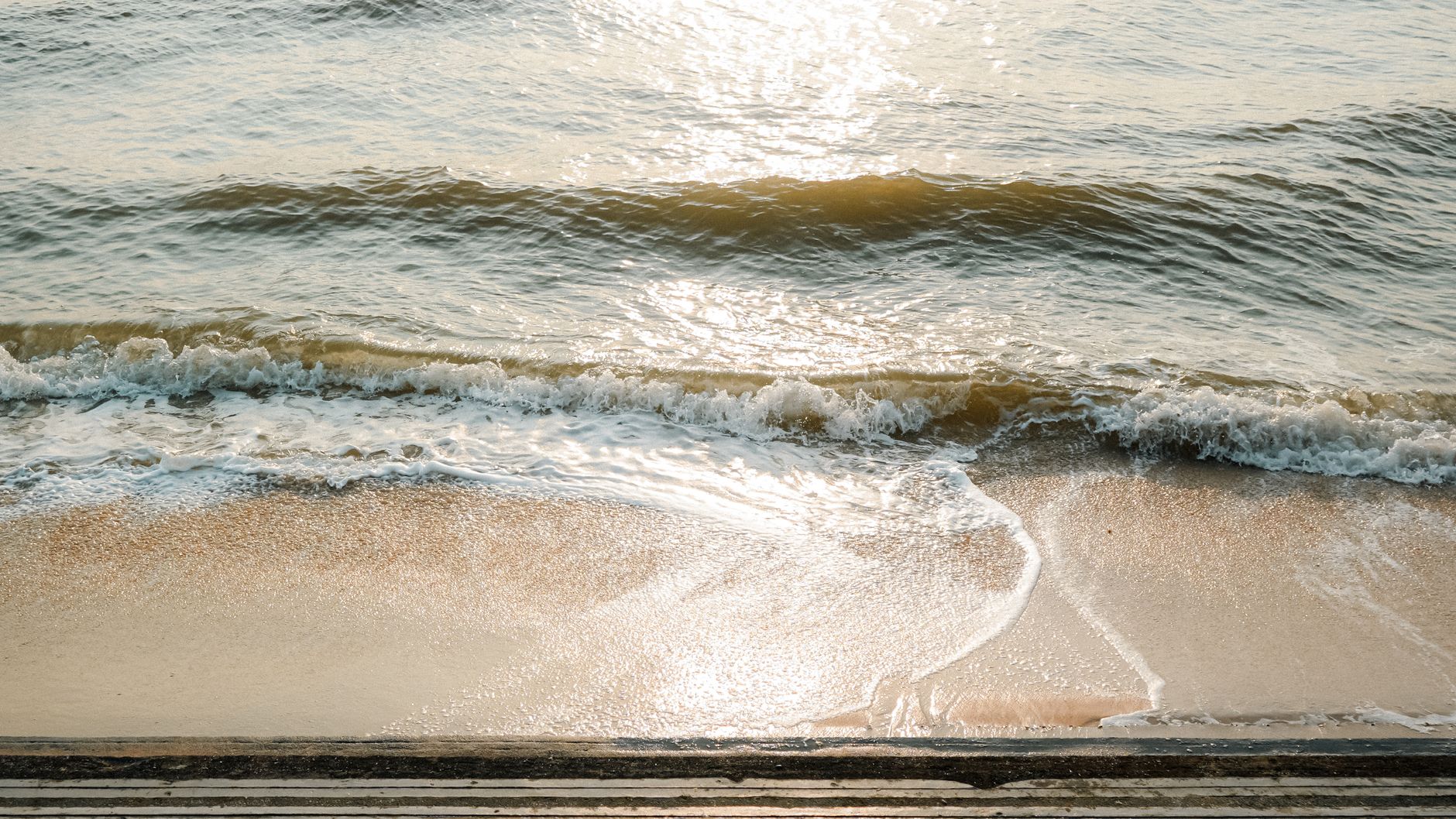 Gentle waves washing onto a sandy beach in warm evening light, with timber steps in the foreground (illustrative stock photo).