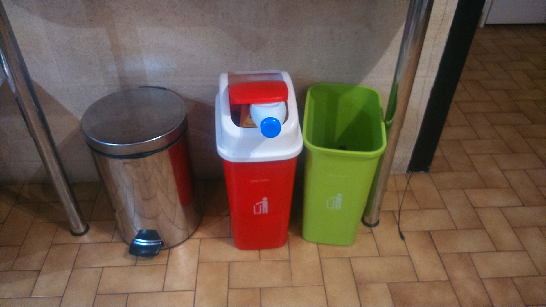 Three small household rubbish bins standing side by side on a tiled floor (illustrative stock photo).